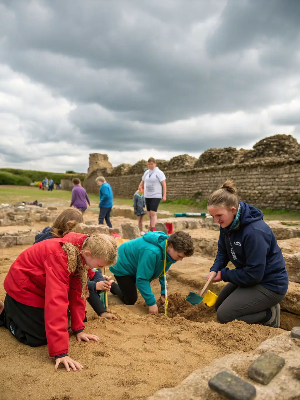 A photograph of children participating in a simulated archaeological dig at a PREHISTOIRE EN HORTE ET TARDOIRE educational program, uncovering replica artifacts in a sandpit.